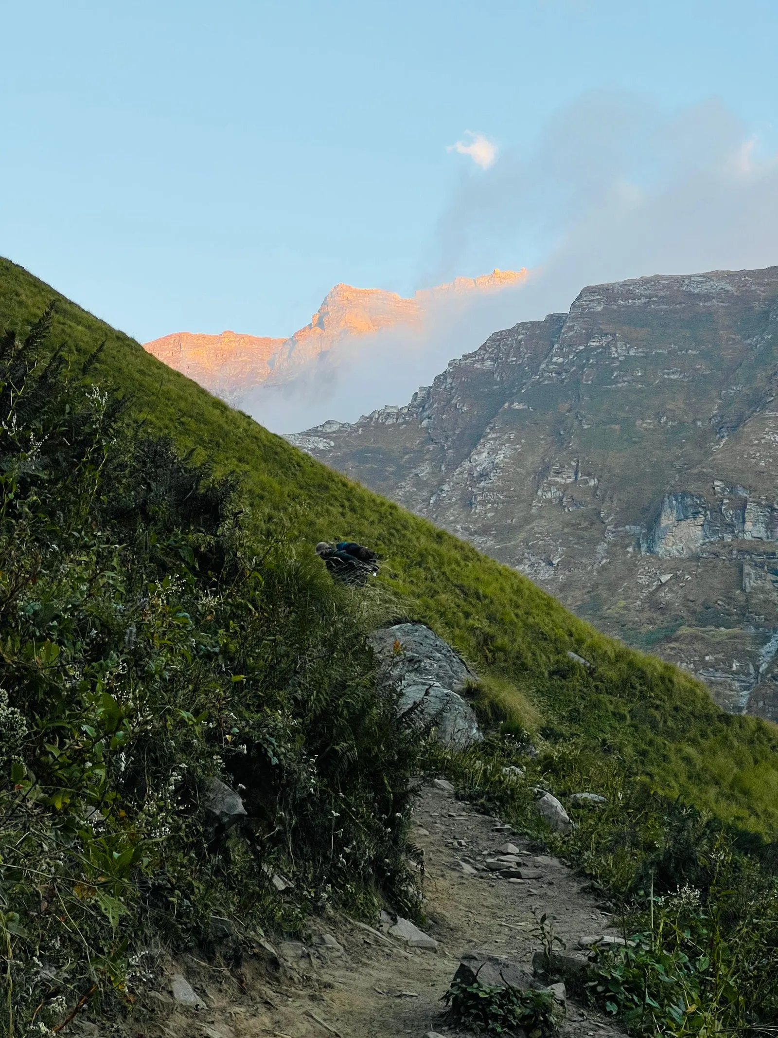 山の斜面に続く登山道と、朝日に照らされた奥の岩山