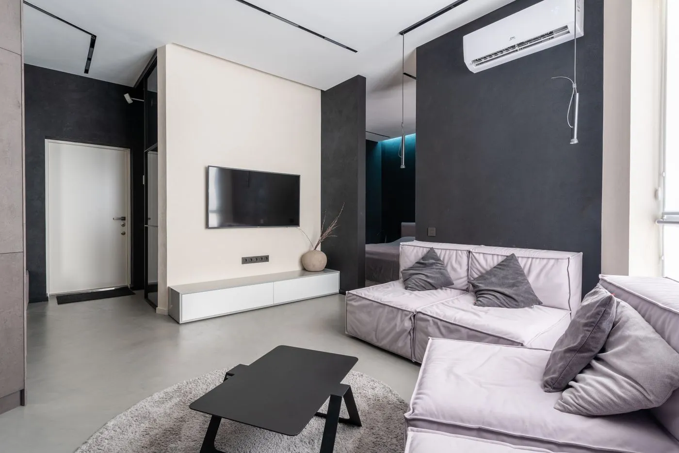 ソファとテレビが置かれた広い居室。壁の上部にエアコンがあり、奥の部屋へ続いている