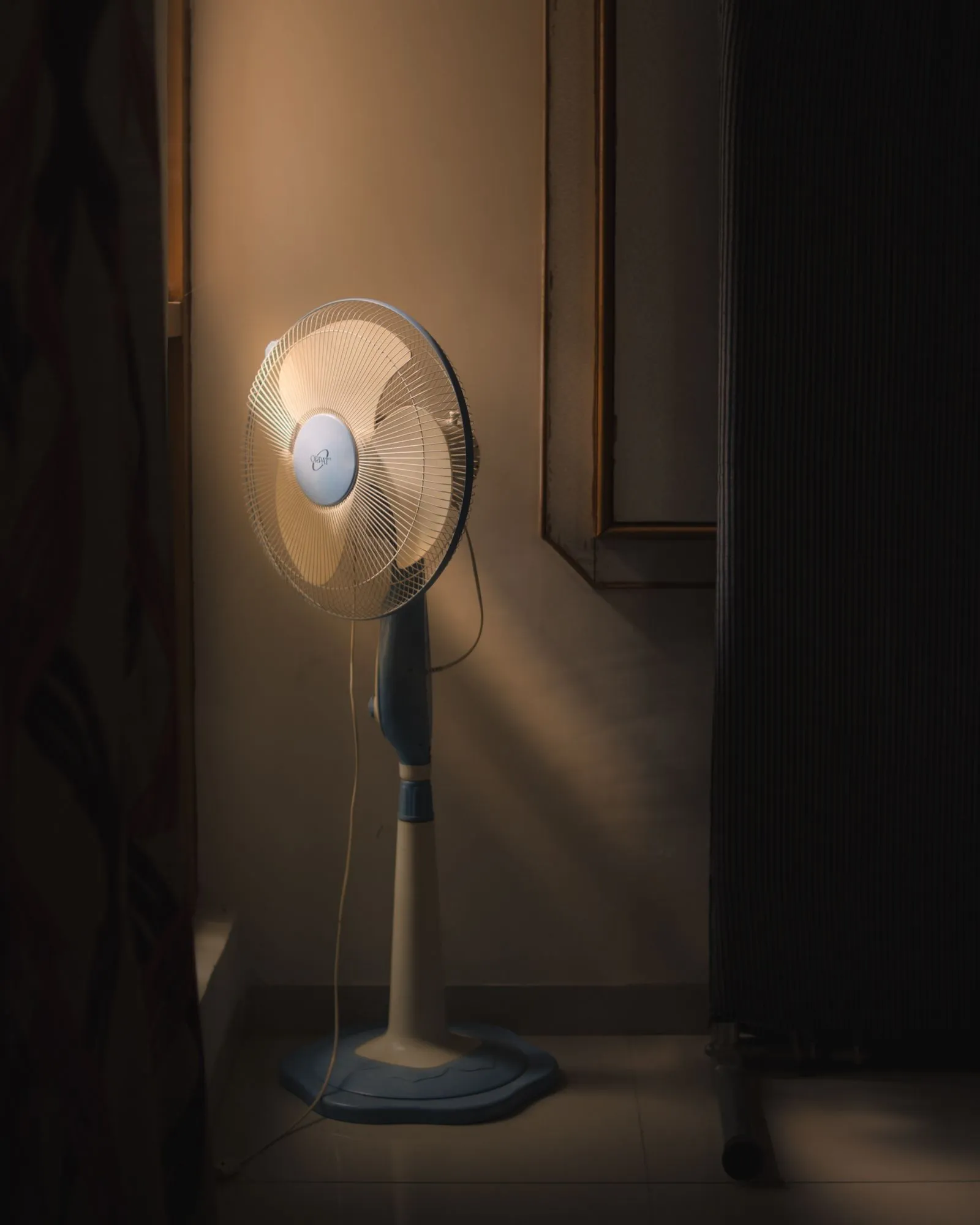 暗い部屋の壁際でほのかに照らされた扇風機