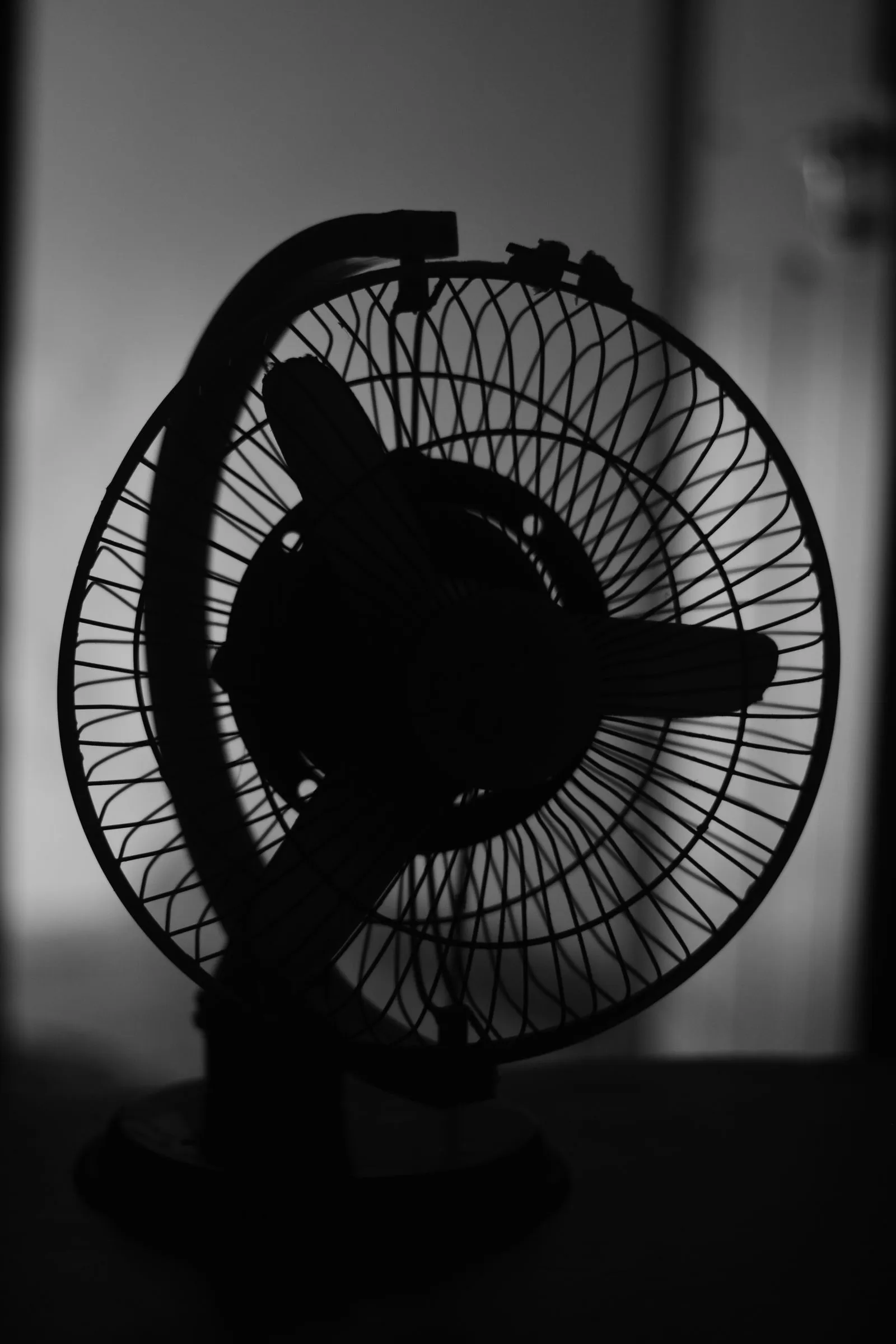 白い壁を背に黒いシルエットで浮かぶ扇風機