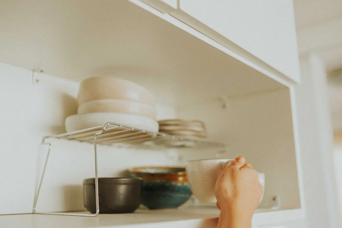 吊り戸棚の中に手を伸ばして、重ねた器を取り出そうとしている