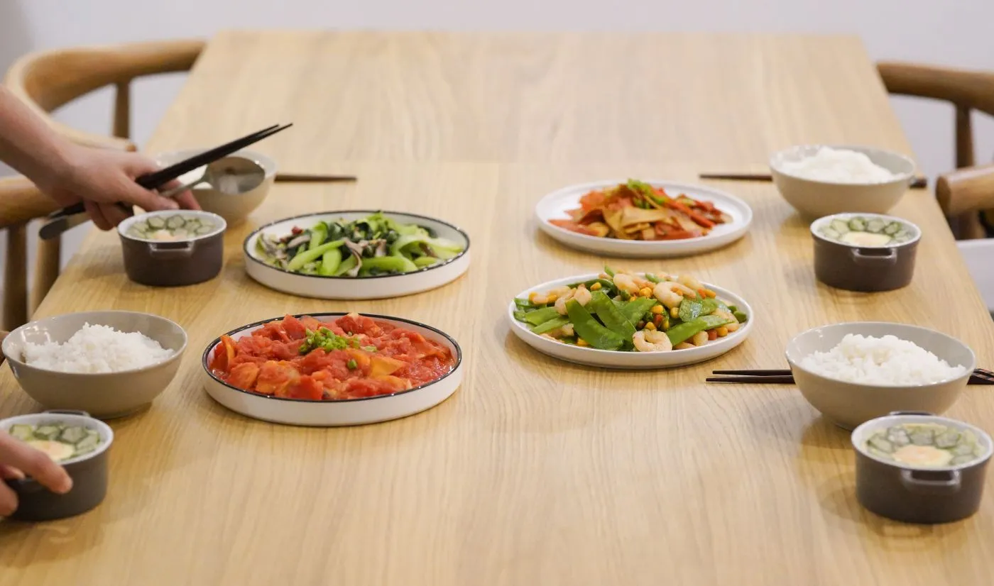 木のテーブルに、大皿の料理数品とご飯茶碗が人数分並んでいる