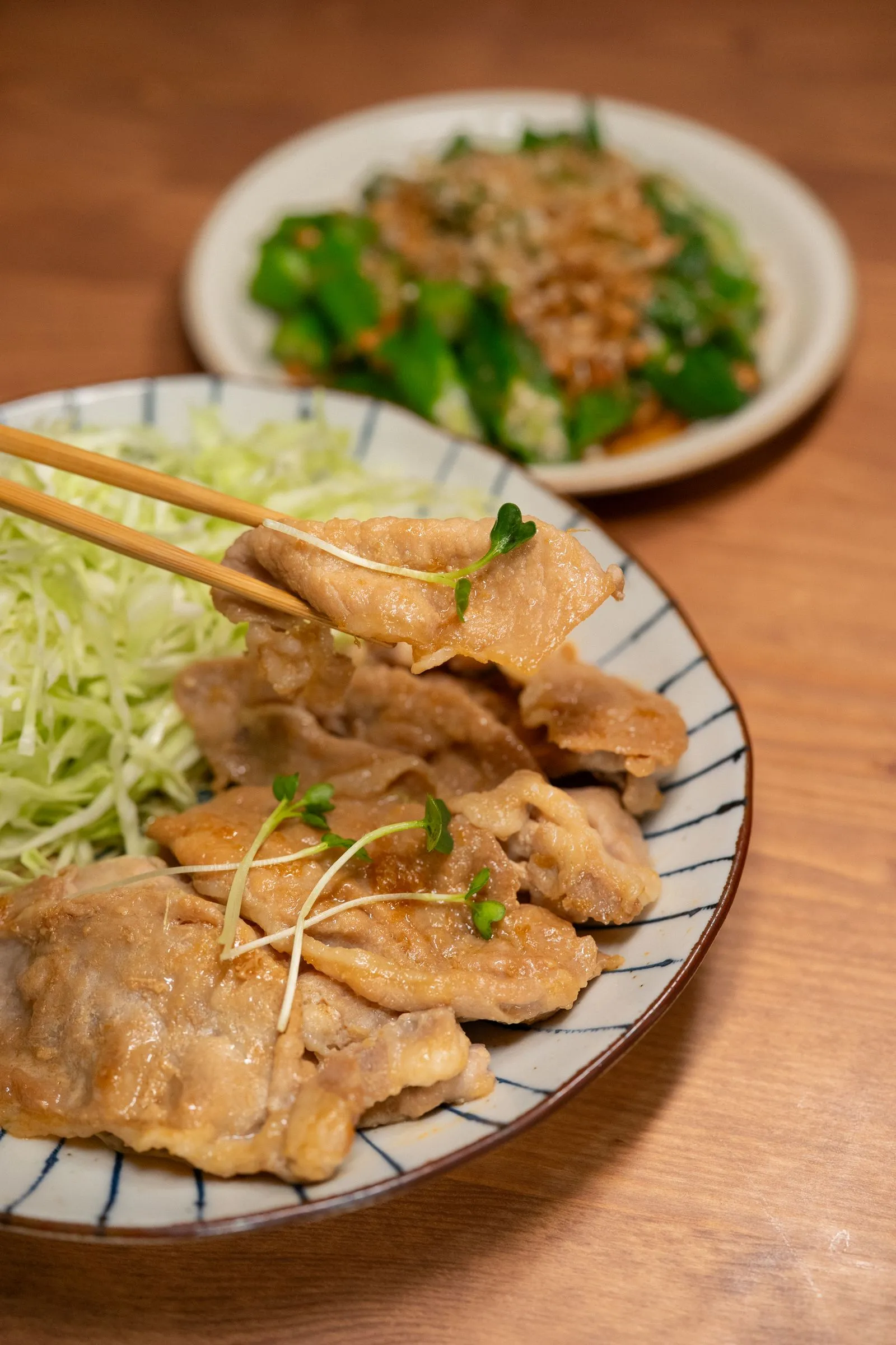 箸でつまむ豚肉料理と千切りキャベツ