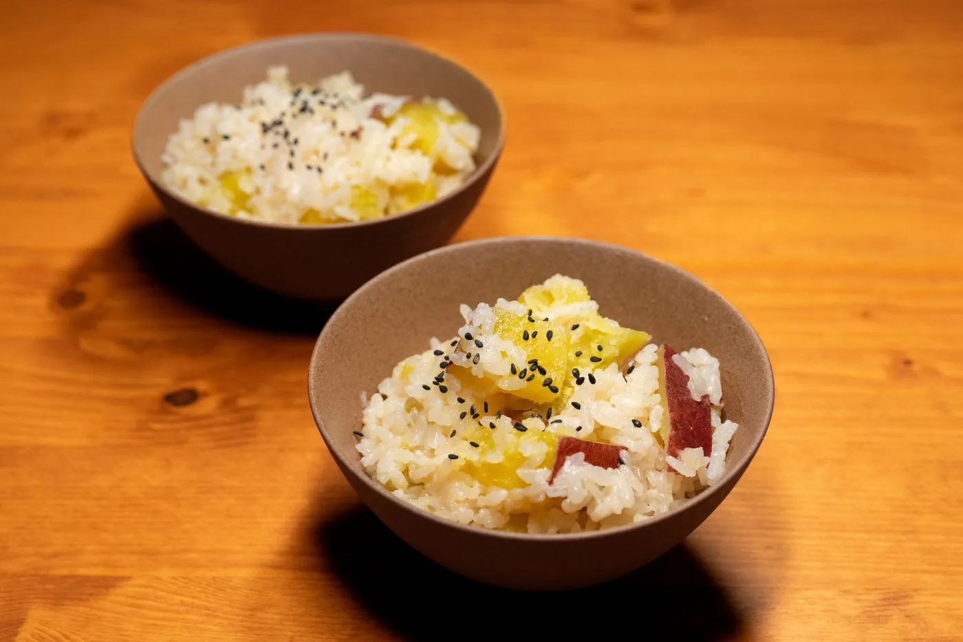 木のテーブルに、さつまいもの入ったご飯を盛った茶碗が2つ置かれている
