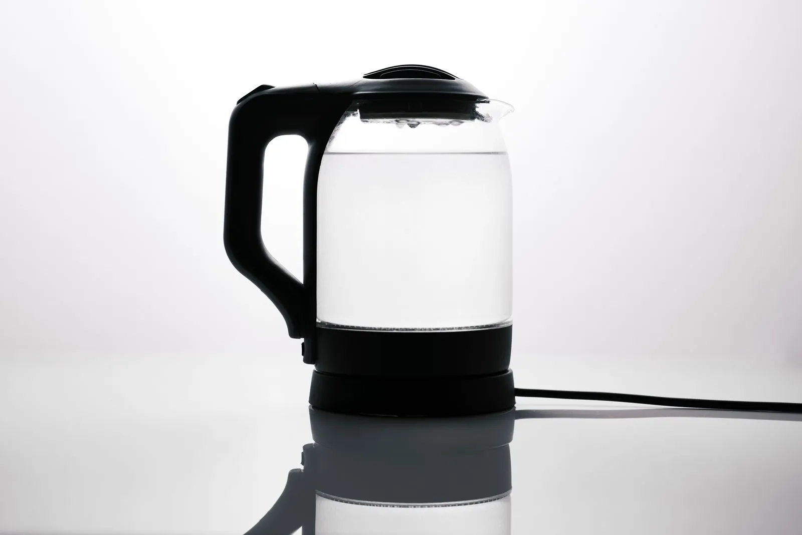 ガラス製の電気ケトルに水が入り、光沢のある台の上で反射している