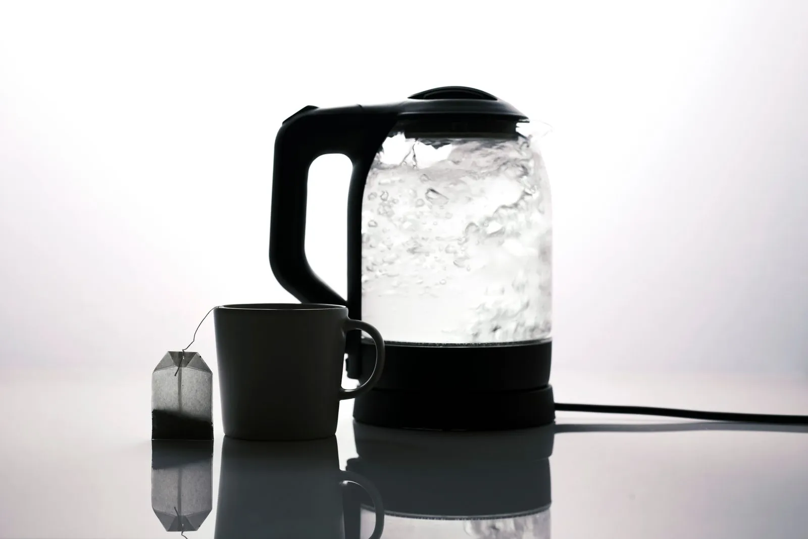 白い背景に電気ケトルとティーバッグの入ったマグカップのシルエットが写っている