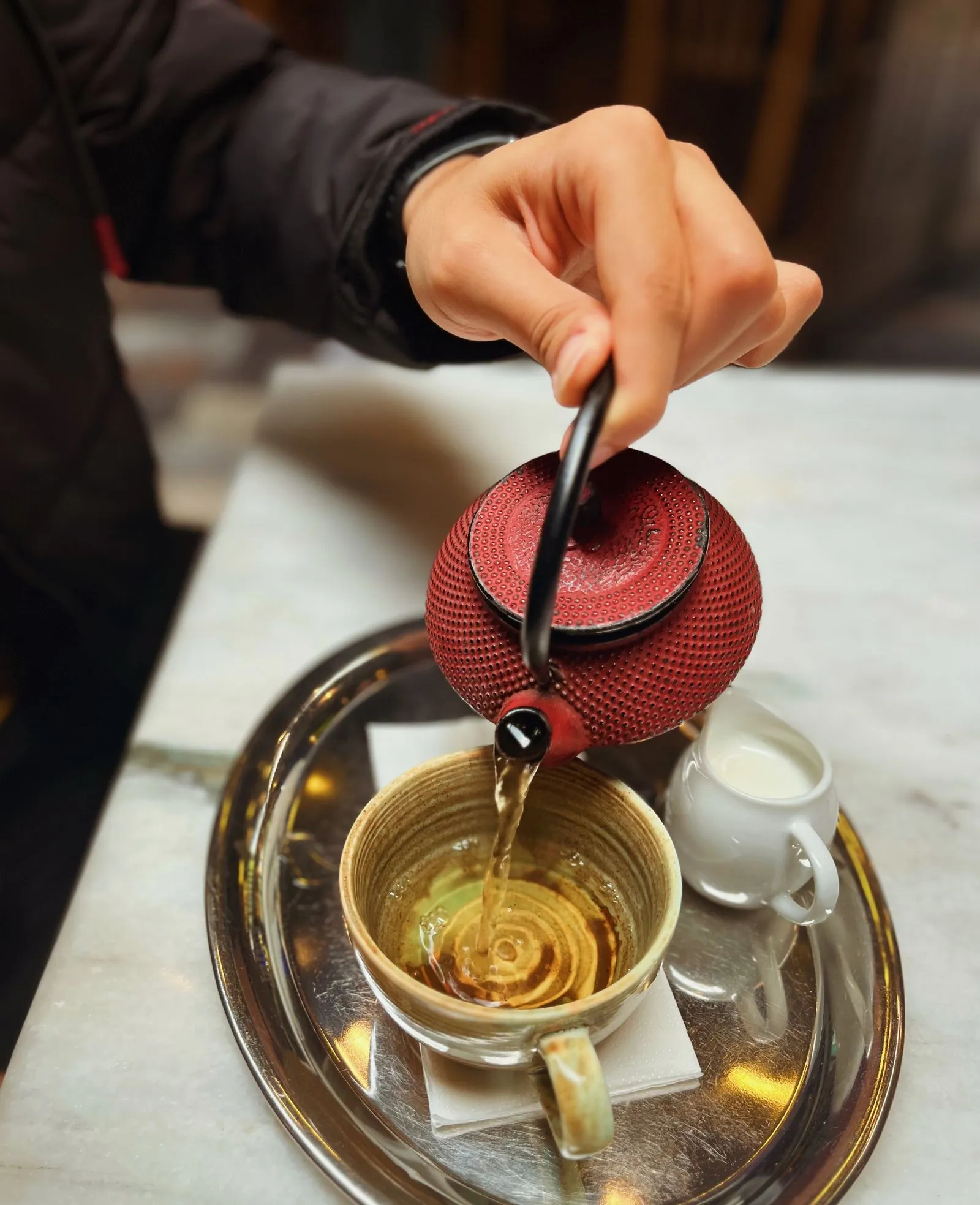 トレーの上でカップに湯を注ぐ赤い鉄瓶
