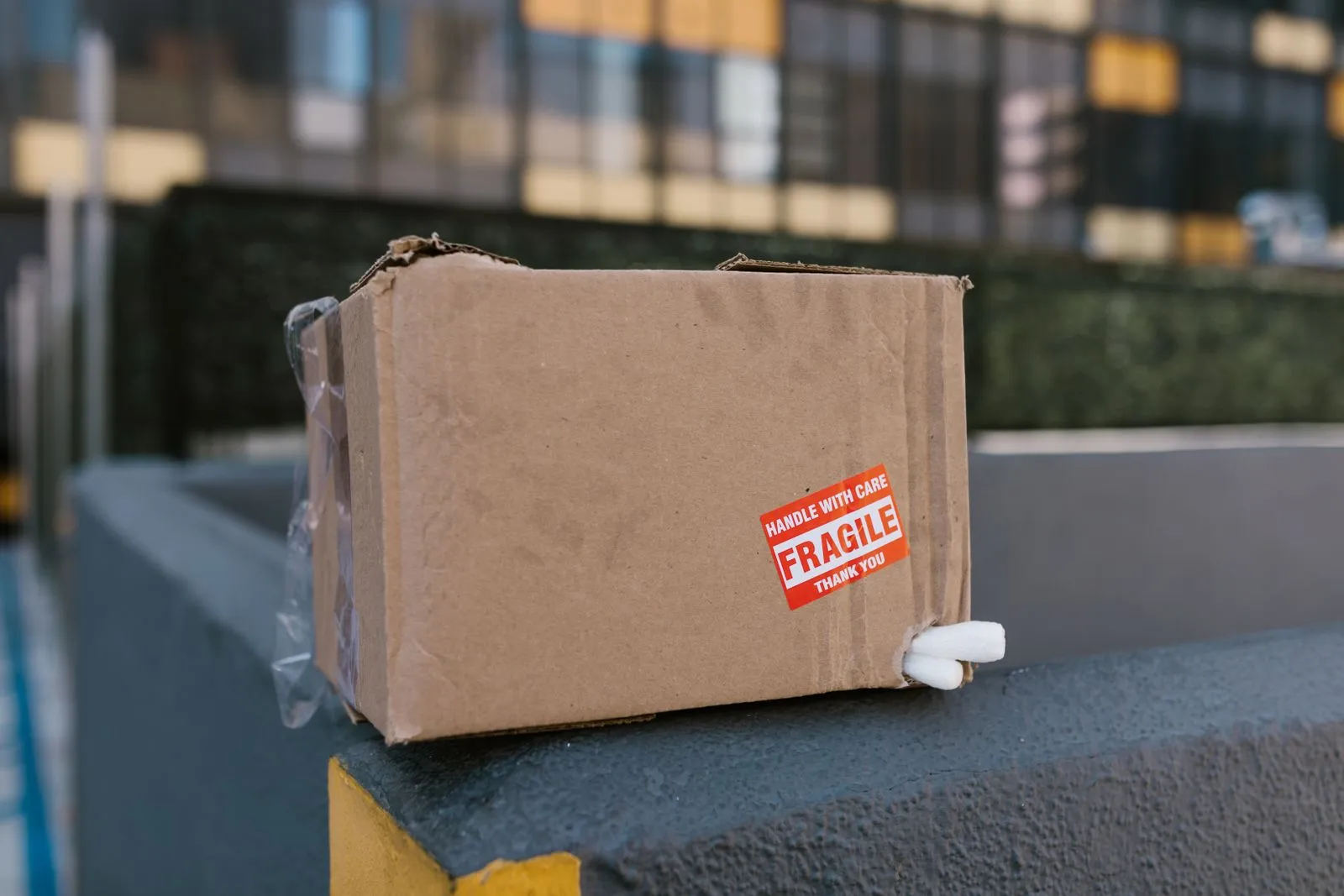 「HANDLE WITH CARE / FRAGILE」のシールが貼られた段ボール箱が、コンクリートの縁に置かれている
