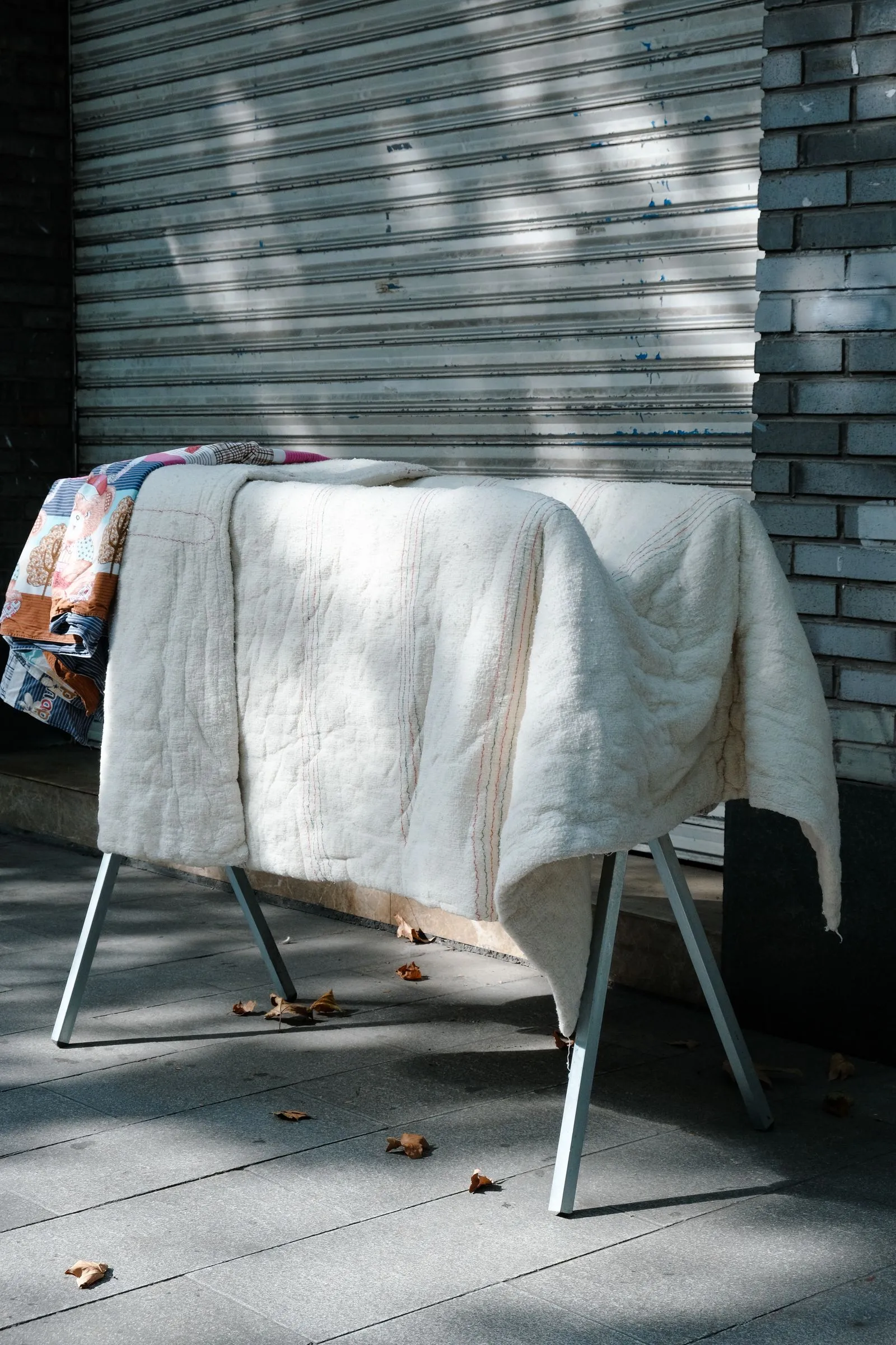 屋外の金属ラックに、白い布団と柄物の布団が重ねて掛けられている