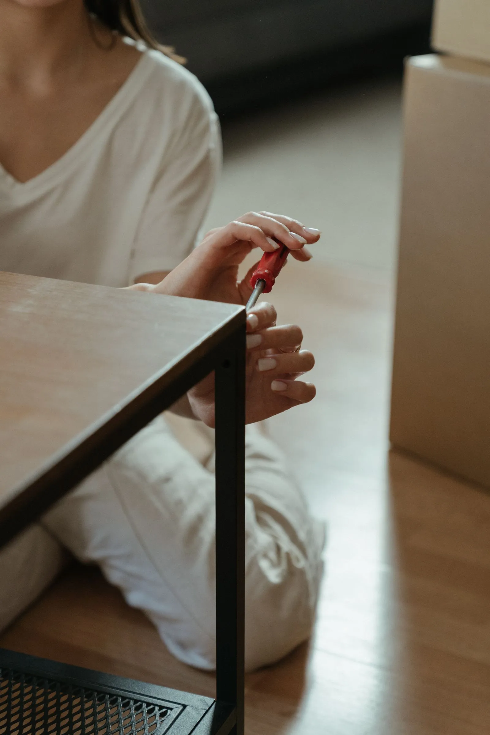 赤い柄の手回しドライバーで、白い服の女性がテーブルを組み立てている