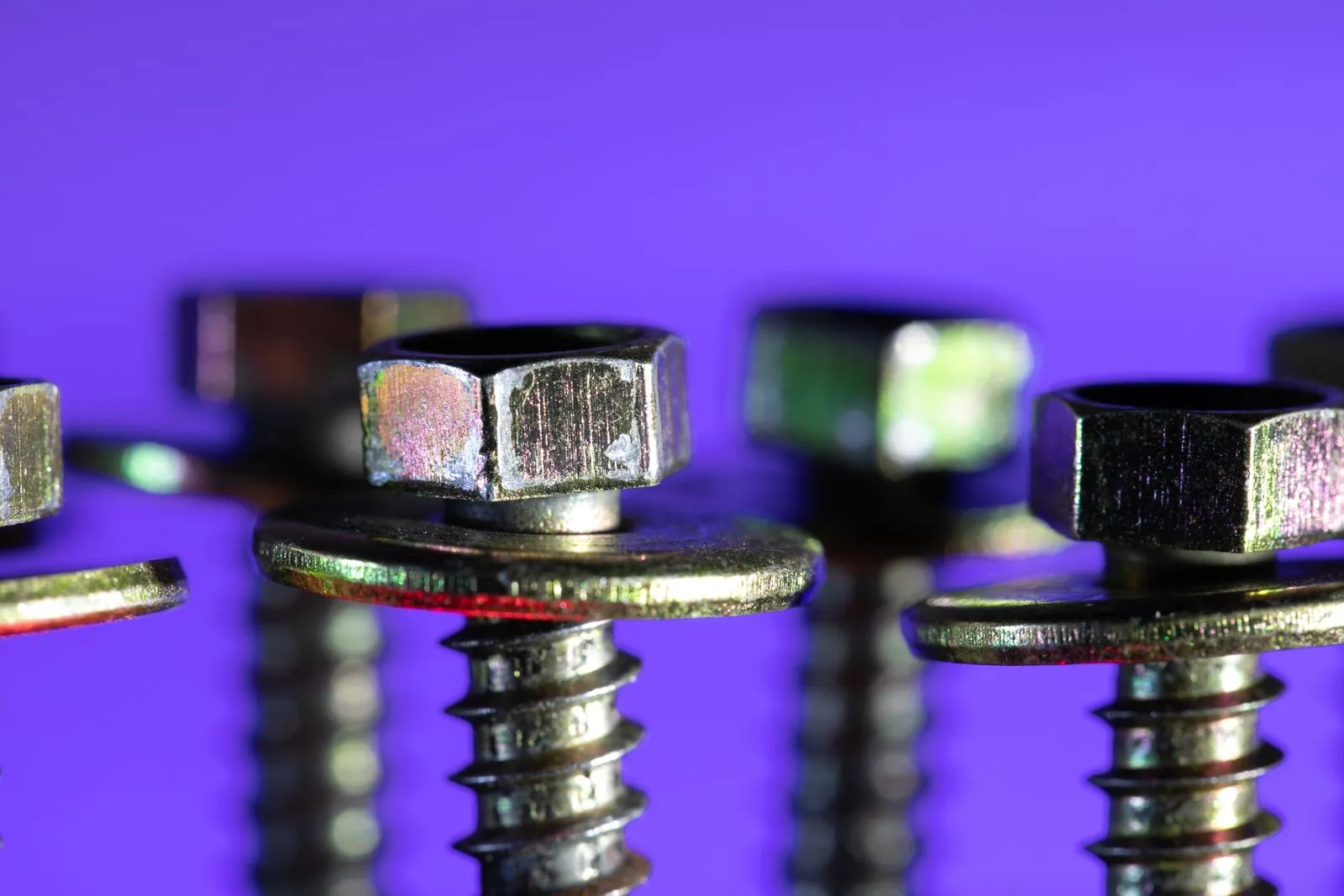 紫色の背景に並ぶ、金属製のねじとナット