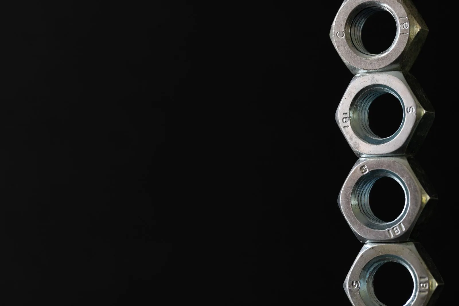 黒い背景に積み重なる、4つの六角ナット