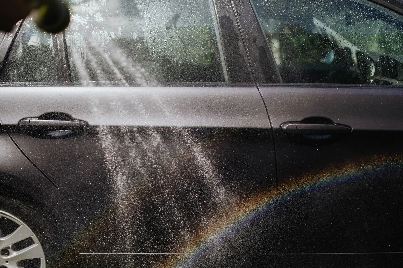 水しぶきを浴びた黒い車のドアに、虹がかかっている