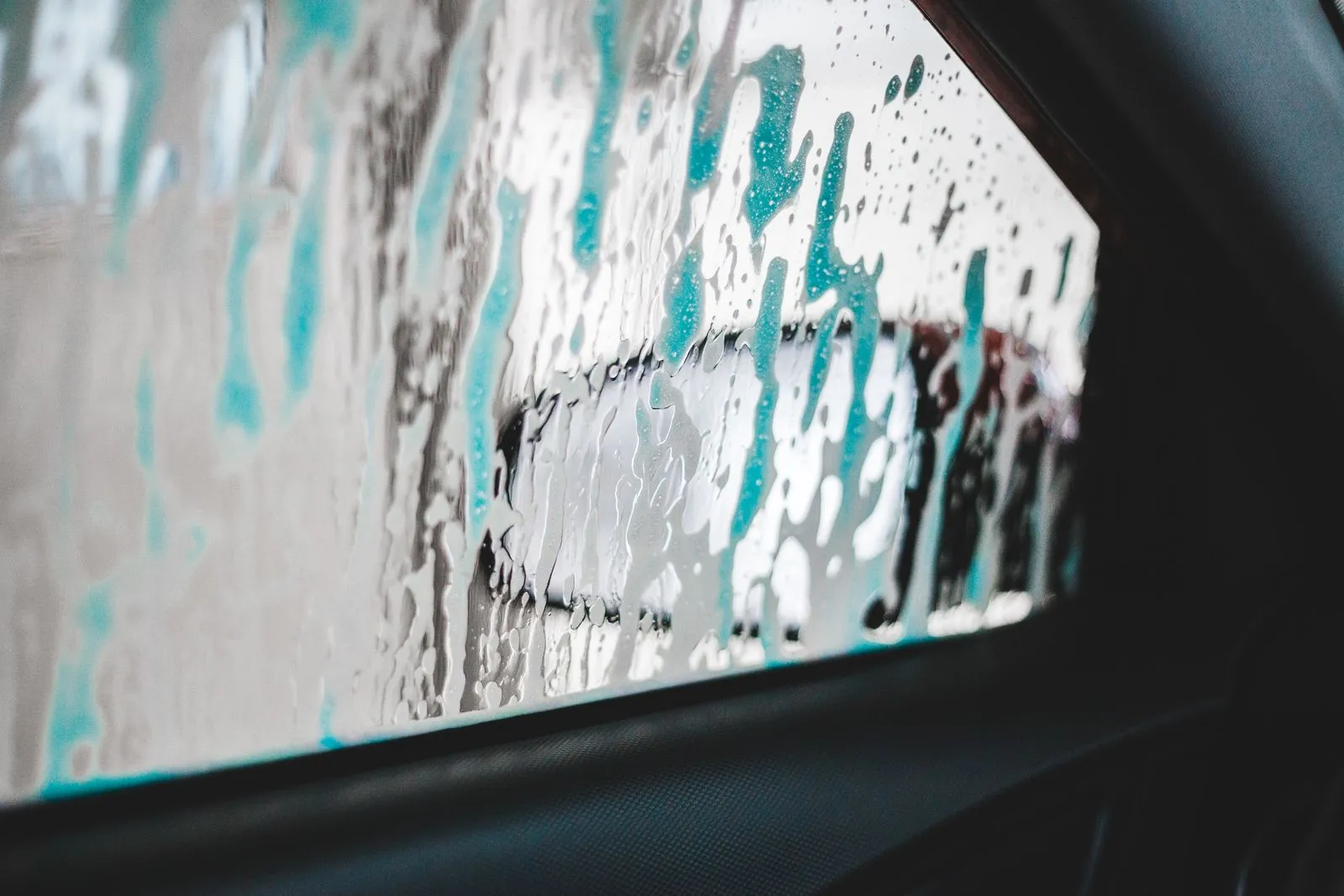 水と泡の筋がついた、車の窓ガラスごしの水色の光