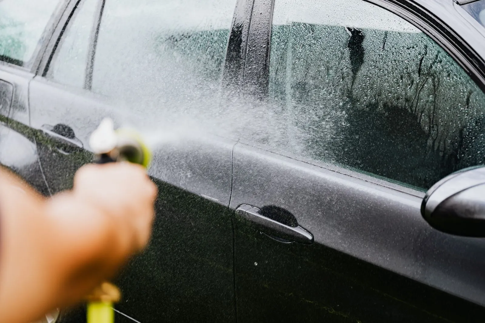 水滴の付いた車の窓とドアに、ホースの水がかかっている