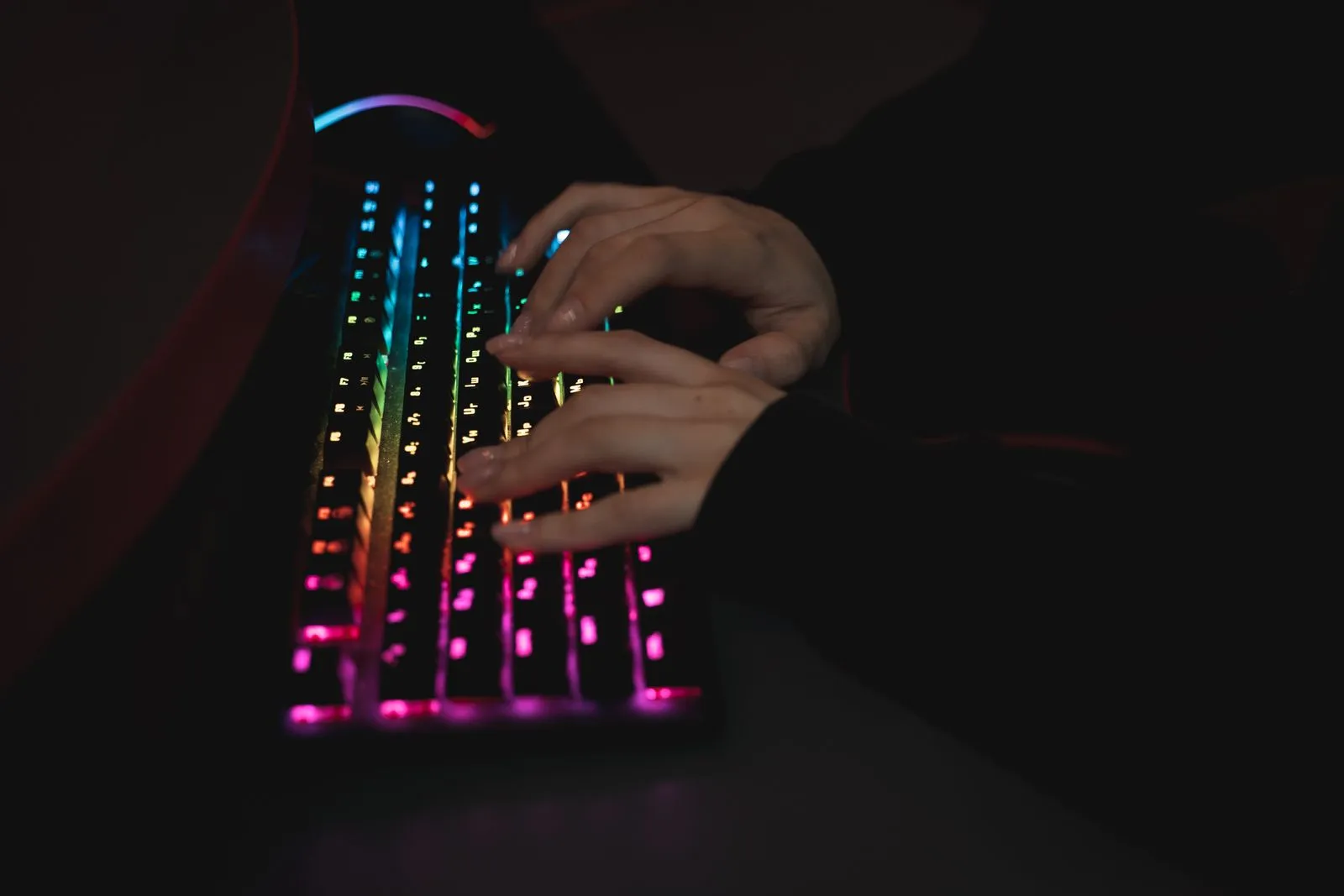 暗い部屋で、虹色に光るキーボードを両手でタイピングしている