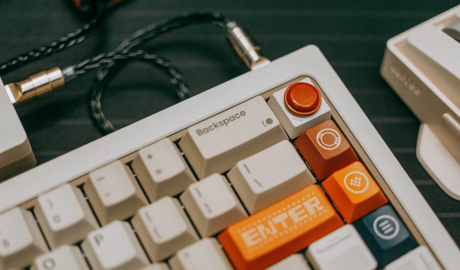 白と黒のキーボードにコイル状のケーブルが接続され、オレンジ色のEnterキーが目立っている