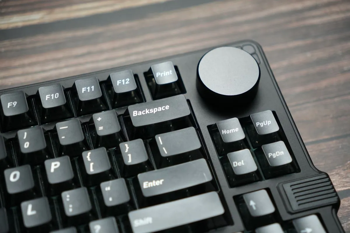 黒いキーボードの角にダイヤル状のノブが付き、木目の机の上に置かれている