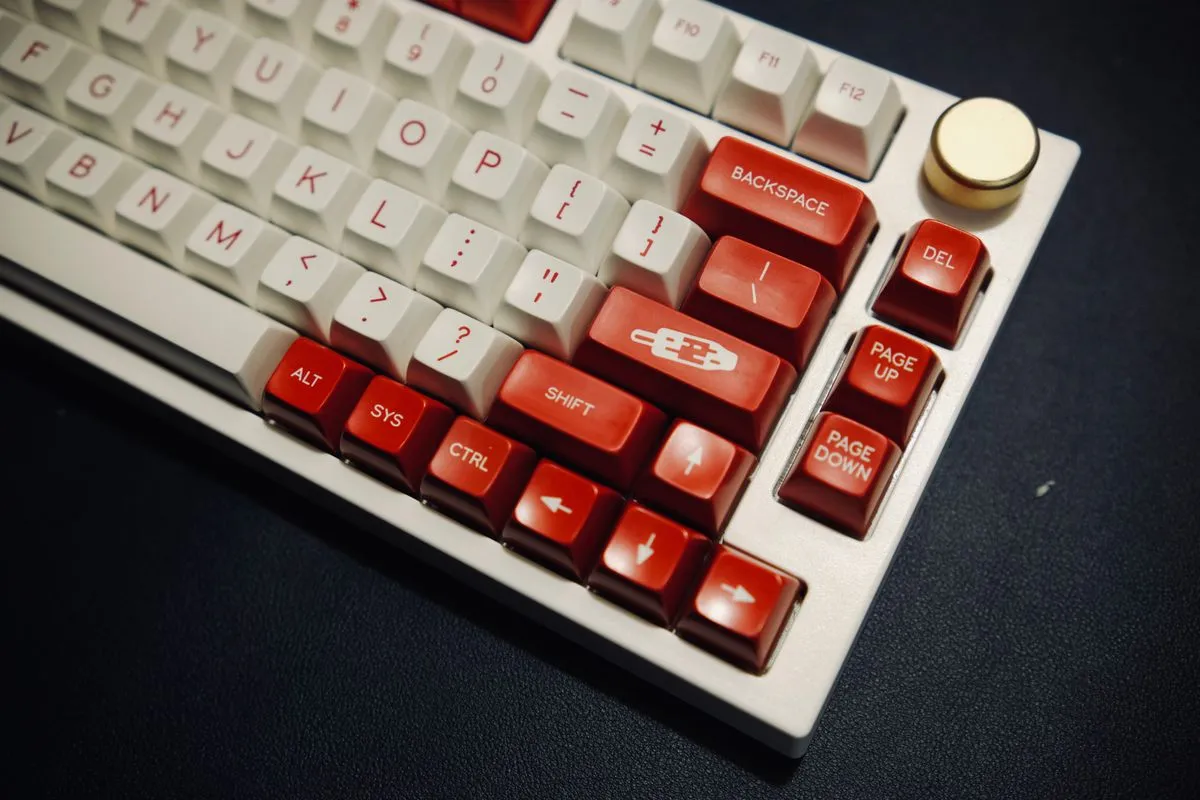 白と赤のキーキャップが並ぶキーボードの手前に、金色の丸いノブが見える