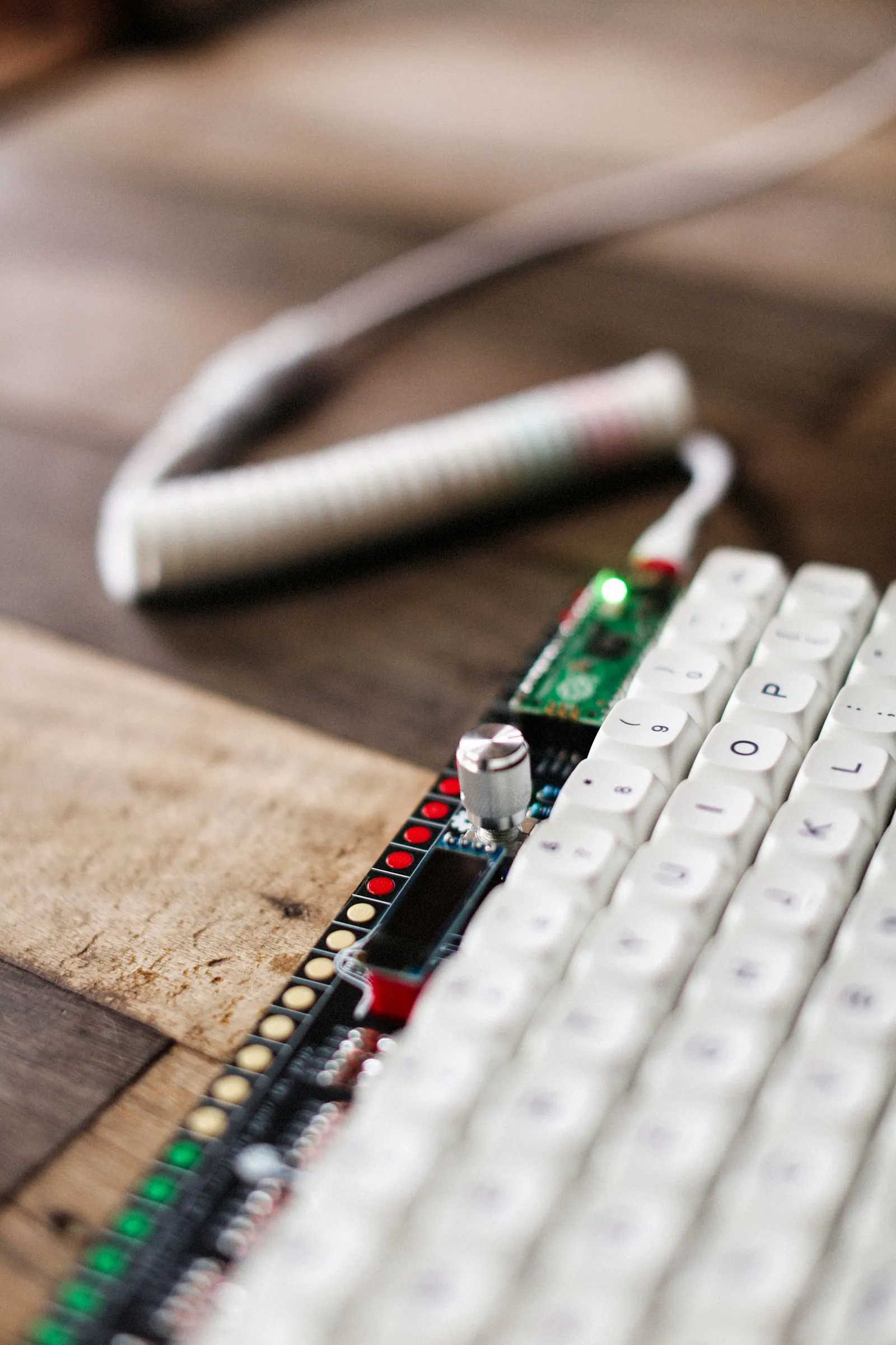 白いキーキャップの列の奥に、赤と緑のLEDが点灯した基板が見えている