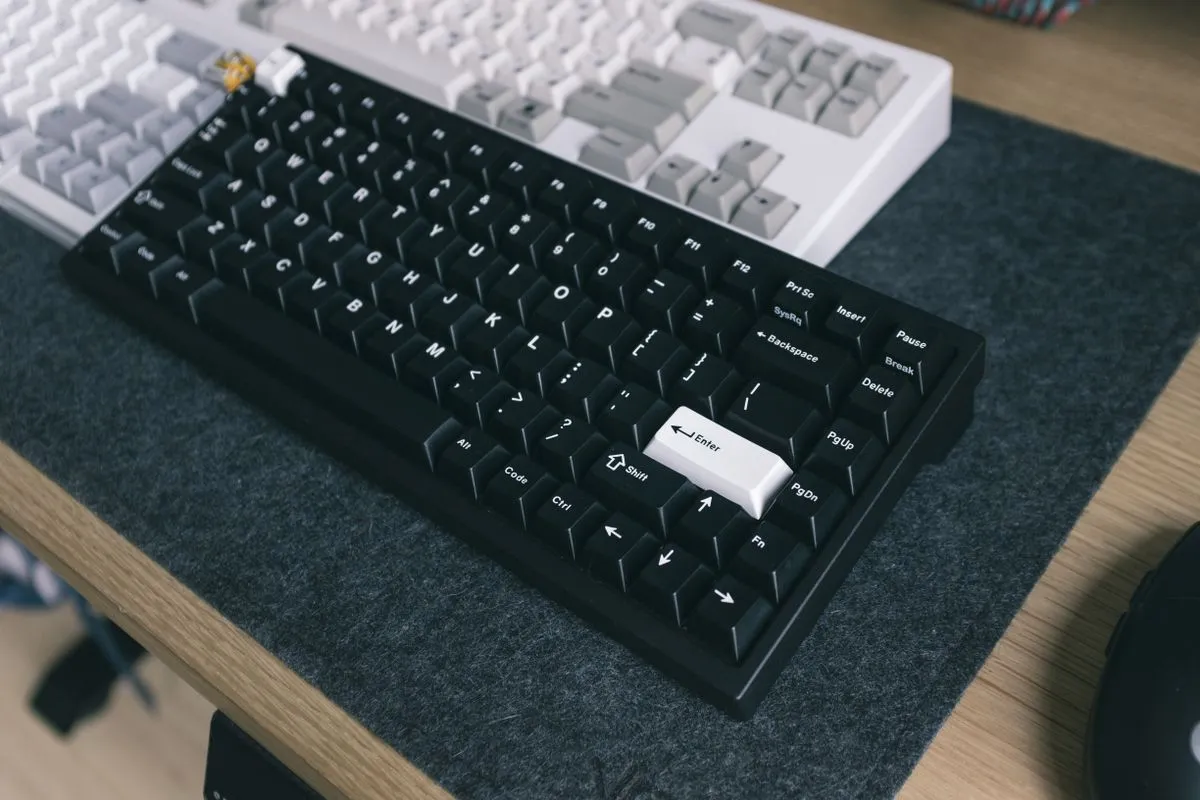 白い壁際の木目の机に置かれたキーボードの上に、両手が乗っている