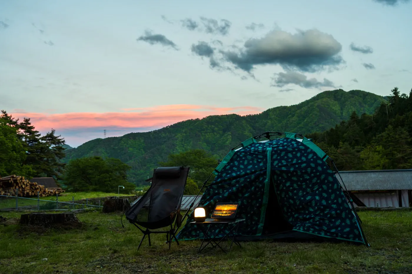 夕暮れの山を背に、草地へ張られたテントと椅子・小さなテーブル