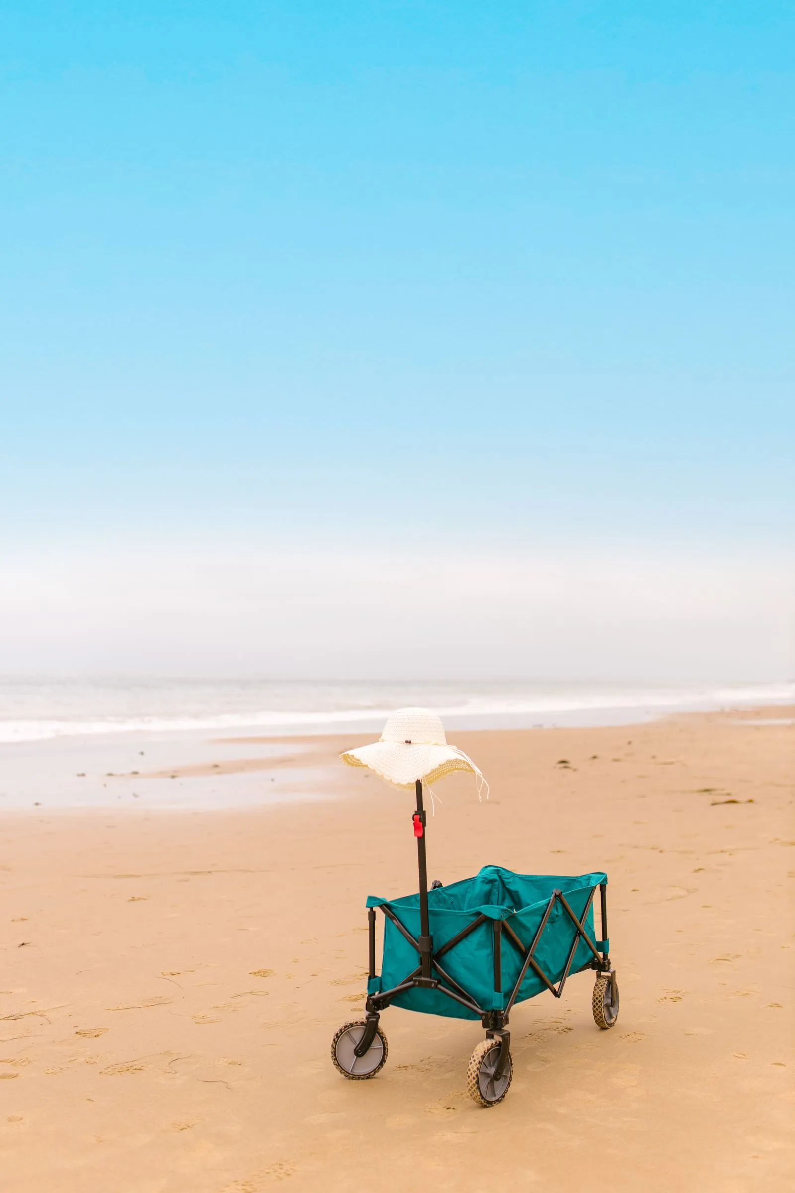 麦わら帽子を飾りとして乗せたワゴンが、人けのない砂浜に置かれている縦位置の写真