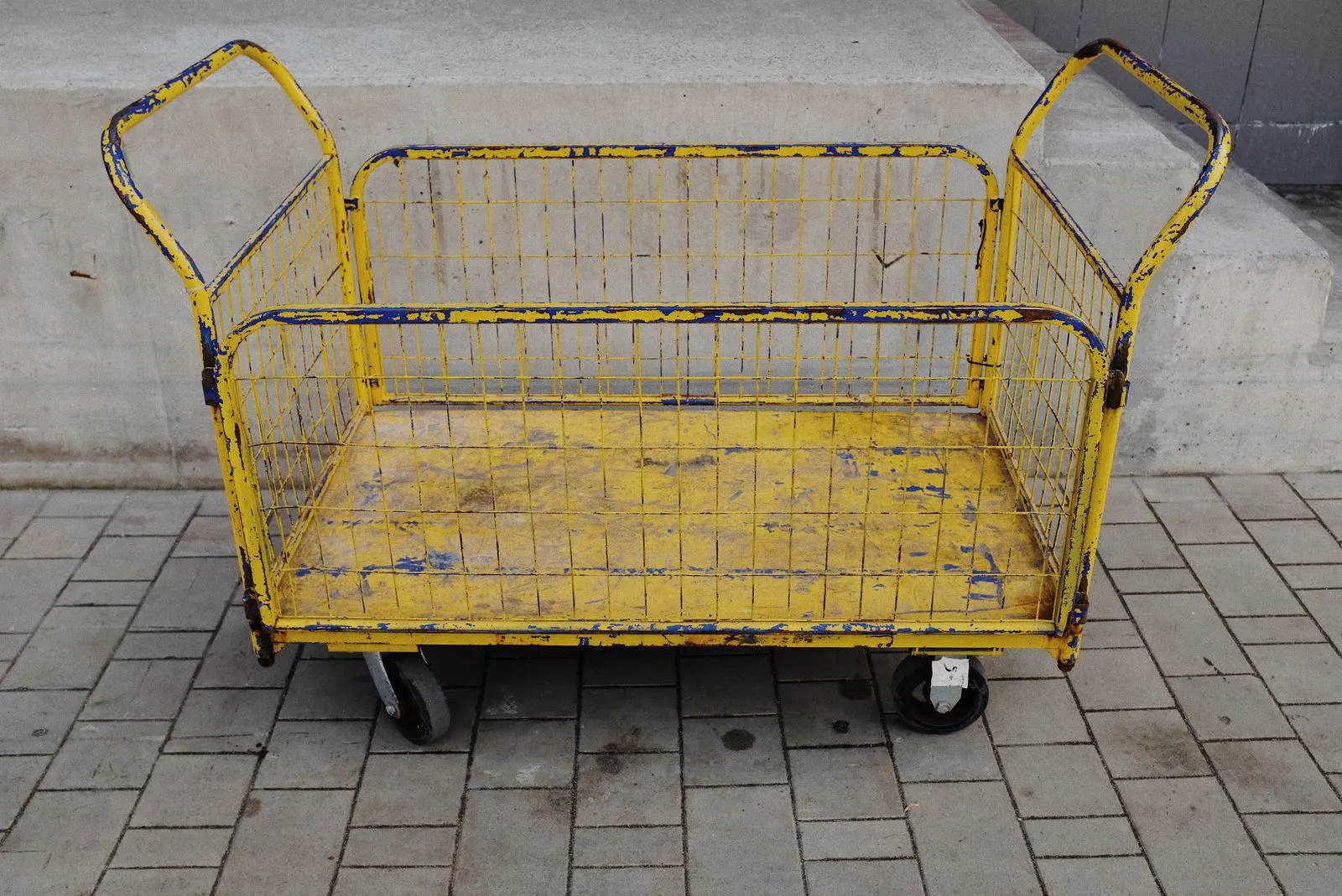 大きなタイヤの黄色いワイヤーカゴ台車が、石畳の広場に置かれている