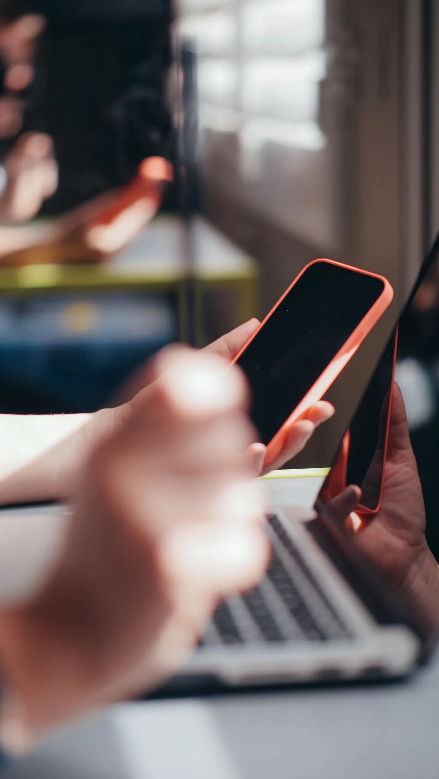 ノートパソコンの前でスマートフォンを操作している手元
