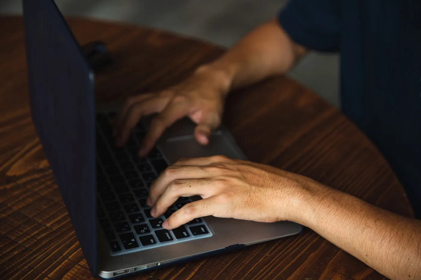 木のテーブルに置いたノートパソコンのキーボードへ両手を置いている